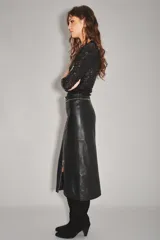 Falda midi de cuero ovino color negro, con diseño de tiro alto y cierre frontal completo con cremallera metálica. Presenta detalles de tachas decorativas a lo largo de la costura central y el borde del cierre.