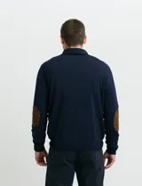 Sweater de punto color verde oliva, con cuello alto y medio cierre frontal. Presenta coderas en símil nappa y puños acanalados.