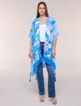 Kimono de gasa azul con estampado botánico de hojas tropicales en tonos celestes, verdes y rosados. Presenta un diseño abierto al frente con mangas cortas y amplias, ruedo asimétrico estilo pañuelo y detalle de borlas en las esquinas inferiores.