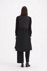 Chaleco largo negro de diseño combinado, con parte superior en matelassé y parte inferior de tela lisa. Presenta cuello alto con cordones ajustables y cierre frontal completo.