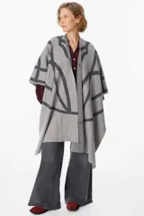 Ruana de tejido de punto con diseño geométrico de líneas curvas en tonos beige y visón. Presenta una caída fluida y envolvente, ideal para usar como capa sobre otras prendas.