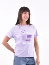 Remera de manga corta color lila, con estampado frontal en violeta que incluye una botella de soda, un vaso de vermut con rodajas de cítricos y aceitunas, y el texto "amor, gentío y vermut bien frío".