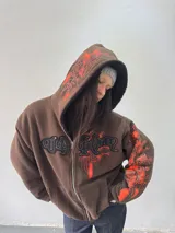 Campera reversible con cierre frontal. Un lado confeccionado en algodón color marrón con estampa plastisol en color naranja, bordados con apliques y capucha. El otro lado confeccionado en tela polar de pelo largo color negro con capucha.