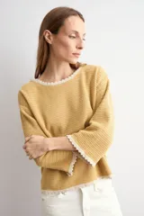 Sweater de punto negro con escote bote, mangas largas y detalles de terminación en ondas de color blanco en el cuello, los puños y el ruedo.