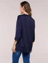 Camisa de satén azul marino con cuello mao, escote en V y mangas tres cuartos con hombro caído. Presenta silueta holgada, cierre frontal con botones y ruedo asimétrico.