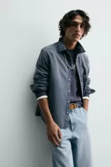 Camisa de manga larga con cuello solapa, bolsillo de plastrón en el pecho y cierre frontal con botones a presión. Presenta un patrón de cuadros vichy en tonos de azul desgastado.