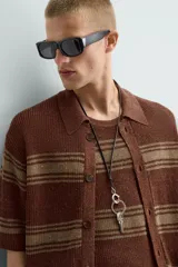 Camisa de punto de manga corta, color marrón rojizo con rayas horizontales en tono beige/verde oliva. Presenta cuello solapa y cierre frontal de botones.