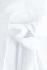 Vestido camisero corto color blanco, de manga corta, con botones metálicos frontales, cuello camisero, falda circular y cinturón de la misma tela para anudar en la cintura.