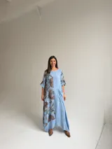 Vestido largo celeste con gran estampado floral marrón en el lateral derecho, de corte holgado, mangas 3/4 con trabilla y dobladillo irregular con flecos desflecados. Incluye un bolsillo aplicado en el frente.