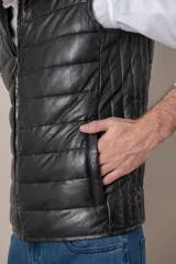 Chaleco de cuero negro con cierre frontal y cuello mao. Diseño acolchado horizontal.