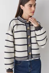 Cardigan de lana color bordó con cuello redondo, cierre frontal de botones y mangas largas. Presenta detalles de ribetes en contraste en cuello, puños y borde inferior, además de un bordado de raqueta de tenis en el pecho.