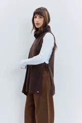 Poncho asimétrico de tejido de punto en color marrón, con cuello alto tipo polera y diseño sin mangas con aberturas laterales.
