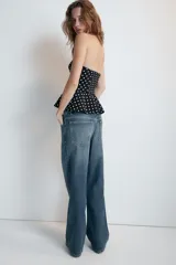 Top de escote recto y hombros descubiertos, color negro con estampado de lunares blancos. Presenta diseño entallado con bajo acabado en peplum y cierre lateral con cremallera oculta.
