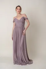 Vestido largo de fiesta color lila, confeccionado en gasa. Presenta un corsé drapeado con escote off-shoulder y mangas caídas. La falda es amplia y fluida.