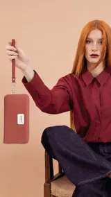 Billetera larga con cierre perimetral, confeccionada en material sintético texturizado color mostaza. Cuenta con correa de mano extraíble y placa metálica con logo de la marca en el frente.