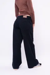 Pantalón wide leg de tiro bajo en color negro, confeccionado en denim, con cierre frontal de botón y bolsillos laterales.