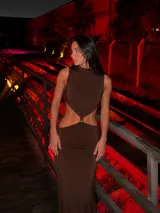 Vestido largo negro con diseño cut-out en la cintura y detalle de hebilla metálica dorada en el centro. Presenta cuello alto y diseño sin mangas.