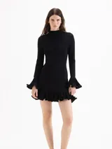 Vestido corto de punto celeste, con silueta ajustada, cuello medio alto y mangas largas. Cuenta con volados plisados en los puños y en el ruedo.