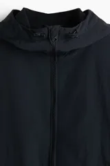 Campera rompevientos de nylon color negro, repelente al agua, con capucha ajustable con cordón, cierre frontal y bolsillos laterales. Cuenta con elásticos en los puños y forro interno.