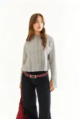 Blusa blanca de algodón con cuello mao y tablas verticales en el frente que crean un efecto de volumen. Presenta cierre frontal con botones y mangas largas.