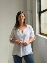 Blusa blanca de lino, con escote en V y tres botones frontales grandes de madera. Cuenta con mangas tres cuartos con presilla y botón para arremangar.