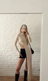 Top de lycra color beige, con cuello alto y mangas largas. Presenta un corte asimétrico en la parte inferior.