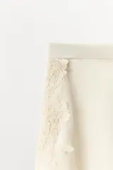 Shorts de tiro alto confeccionado en tejido satinado color verde oliva, con cintura elástica, bajo con volantes y aberturas laterales decoradas con aplicaciones de encaje a tono.
