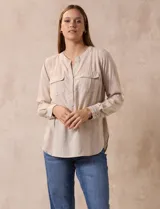 Blusa color beige de lino, marca Dash. Cuello a la base, escote en V y abertura con botones. Delantera con bolsillos. Largo de manga regulable con presilla y botón.