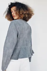 Chaqueta de cuero gamuzado color gris, con cuello redondo, manga larga, cierre frontal con botones oscuros y bajo con detalle peplum.