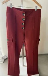 Pantalón cargo de tiro alto color terracota, con cierre frontal de múltiples botones efecto carey y bolsillos laterales cargo con solapa y botón. Presenta costuras verticales decorativas en el frente.