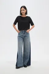 Pantalon de jean de corte ancho con diseño color block, combinando paneles de denim lavado claro en el centro y denim azul oscuro en los laterales. Presenta tiro medio y terminaciones deshilachadas en el ruedo.