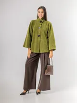 Chaqueta tipo capa confeccionada en paño, con cuello alto, cierre frontal de botones grandes y mangas amplias. Cuenta con bolsillos laterales y forro interior.