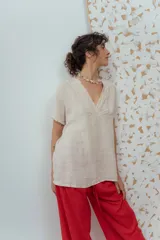 Blusa de lino color beige de calce relajado, con escote en V y detalles de pliegues frontales. Posee mangas cortas y una silueta suelta.