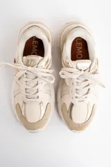 Zapatilla deportiva de diseño urbano en tonos neutros, combinando paneles de malla, gamuza y detalles metalizados en color dorado. Cuenta con suela robusta y acordonado frontal.