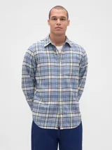 Camisa de manga larga confeccionada en tela de franela con estampado de cuadros en tonos azul claro, blanco y negro. Presenta cuello clásico, cierre frontal con botones y un bolsillo en el pecho.