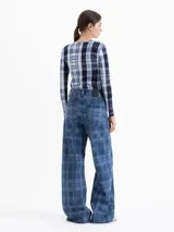 Pantalón de jean de tiro medio y pierna amplia con diseño de cuadros estampados y detalles bordados de flores en contraste. Presenta bolsillos clásicos, cierre frontal con botón metálico y recortes estructurales en las piernas.