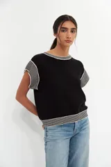 Top de tejido de punto en color negro, con cuello redondo, mangas cortas y detalles de rayas horizontales en blanco y negro en el cuello, las mangas y el ruedo.