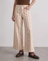 Pantalón de jean tiro alto y corte wide leg, en color beige con estampado vertical de líneas y motivos florales en tono marrón.