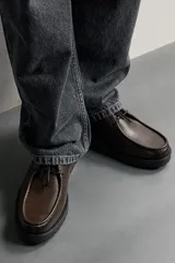 Zapato de cordones de estilo derby, color negro, con parte superior lisa, detalle de bordón en el empeine, horma redonda y suela track dentada.