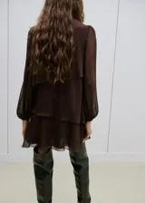 Vestido corto marrón con estampado de lunares, cuello alto y diseño de capas superpuestas con volados. Mangas largas abullonadas semitransparentes.