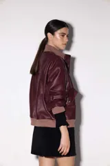 Chaqueta de cuero estilo bomber, con cuello alto, puños y cintura de tejido de punto acanalado. Presenta cierre frontal con cremallera y dos bolsillos laterales con solapa.
