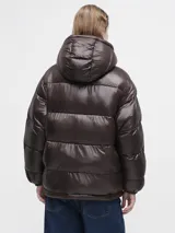 Campera puffer de corte holgado en color marrón oscuro con acabado brillante. Presenta cuello alto, cierre frontal con cremallera y botones a presión, además de bolsillos frontales con solapa.