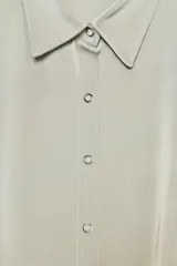 Camisa de satén color verde claro, con cuello solapa, cierre frontal con botones a presión y mangas cortas abullonadas.