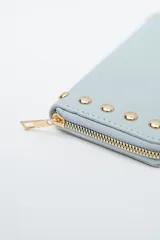 Billetera negra con cierre perimetral y tachas doradas decorativas en el borde frontal.