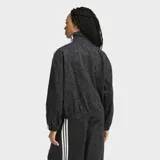 Campera Adidas Firebird AOP extragrande, de tejido denim con estampado animal print en tonos grises y negros. Presenta cuello alto, cierre frontal completo, bolsillos laterales y las clásicas tres tiras blancas de la marca en las mangas.