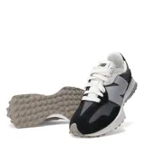 Championes urbanos New Balance modelo 327, con diseño retro que combina paneles de gamuza negra y malla gris. Presenta el logo 'N' sobredimensionado en color gris claro en el lateral, cordones blancos y una suela de goma con relieve que se extiende hacia el talón.