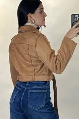 Chaqueta corta tipo biker confeccionada en gamuza color beige, con cierre frontal cruzado, solapas amplias, bolsillos con cierre y cinturón ajustable en la cintura.