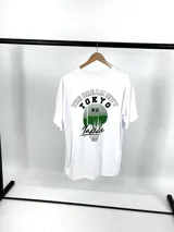 Remera blanca de corte oversize con estampado en el frente con la leyenda "The Dream City Tokyo Japan" en letras negras y un diseño de skyline en verde.