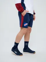 Bermuda deportiva Umbro del Club Nacional de Football, color azul marino, con cordón ajustable en la cintura, bolsillos laterales, el escudo del club en una pierna y el logo de la marca en la otra.