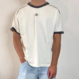 Remera de corte regular color blanco con detalles en gris oscuro en el cuello y los bordes de las mangas. Presenta un estampado pequeño centrado en el pecho.